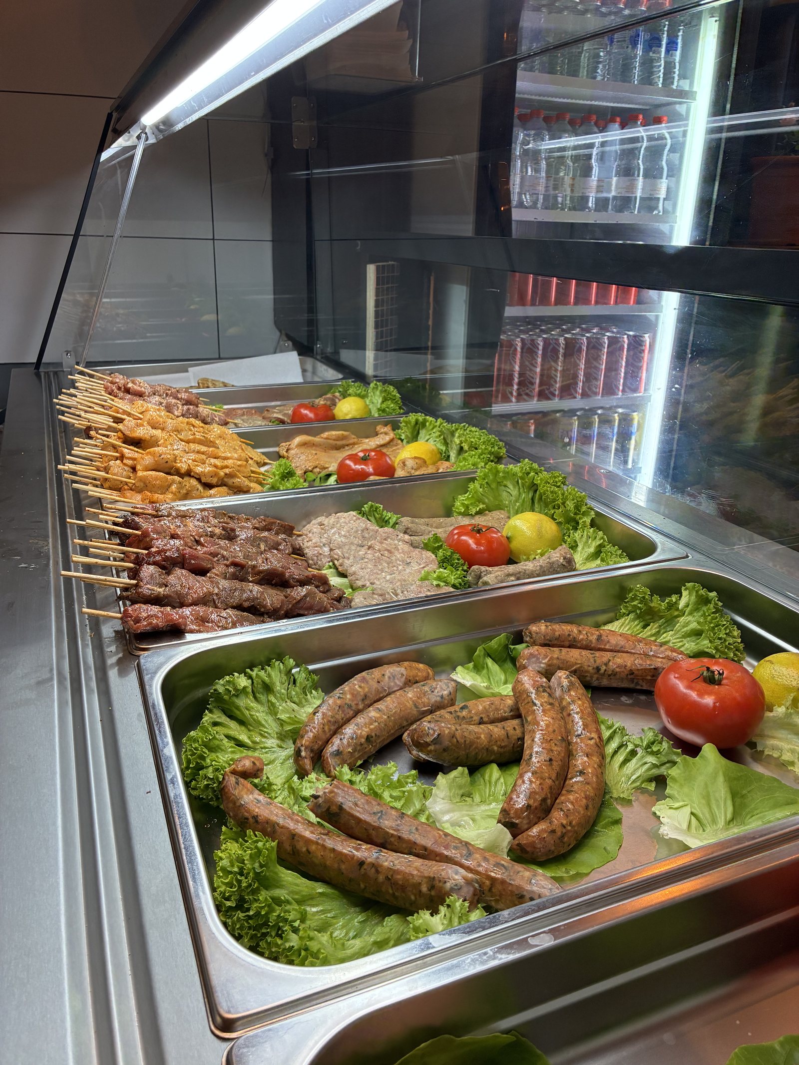 Fresh meat display at ESTIA with handmade skewers, sausages, patties, lettuce, tomatoes and lemons